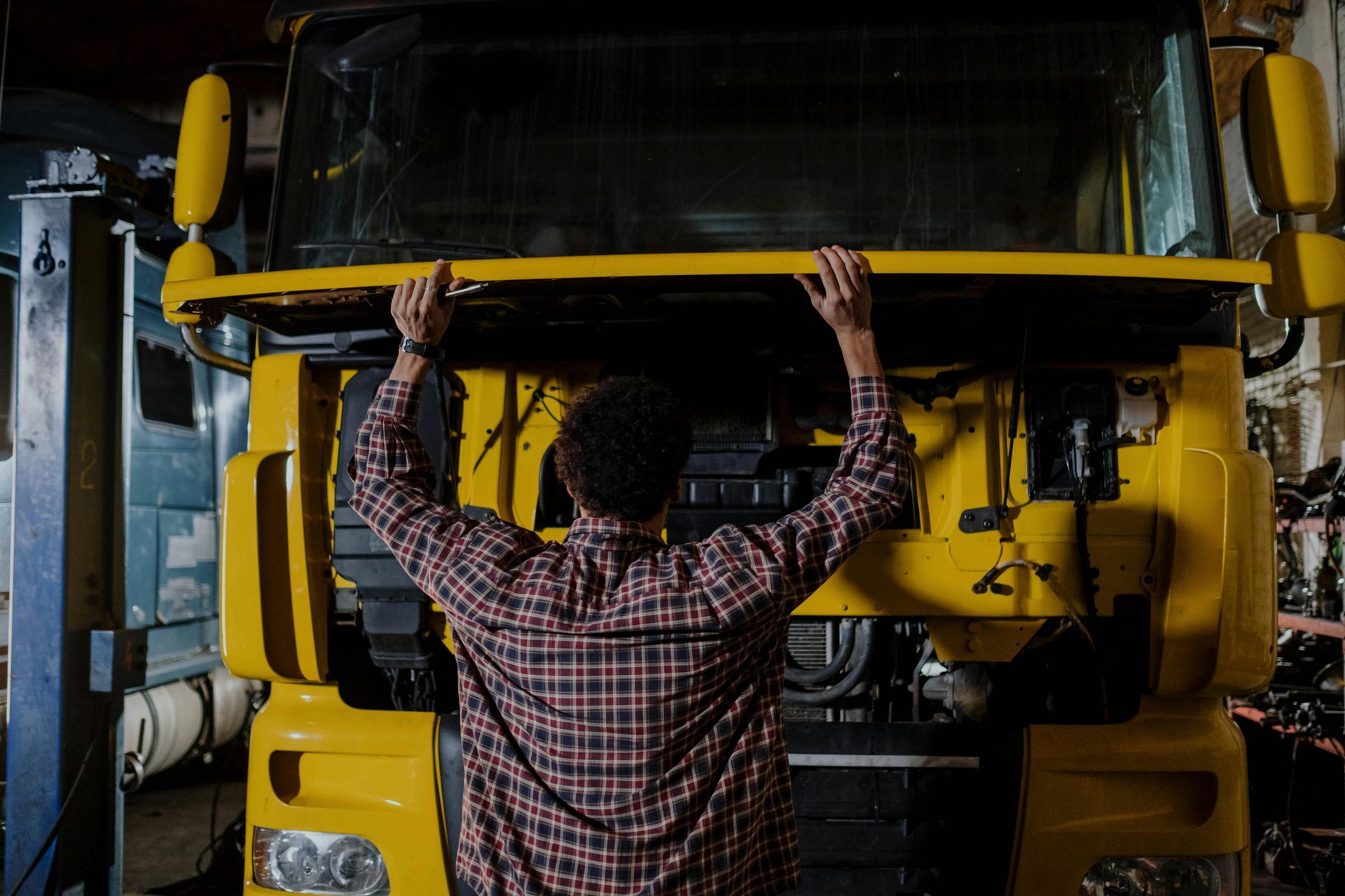 Person in plaid shirt working on a yellow truck in a junk removal garage.