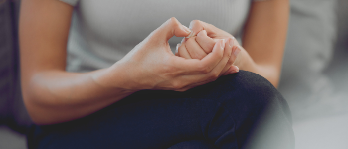 A woman is sitting on a couch with her hands showing signs of anxiety.