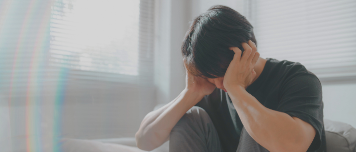 A man is sitting on a couch with his head in his hands.