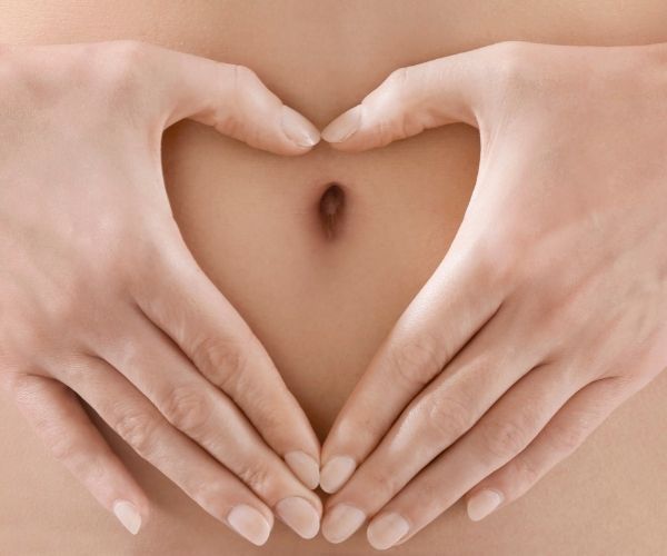 woman with hands held over stomach in heart shape