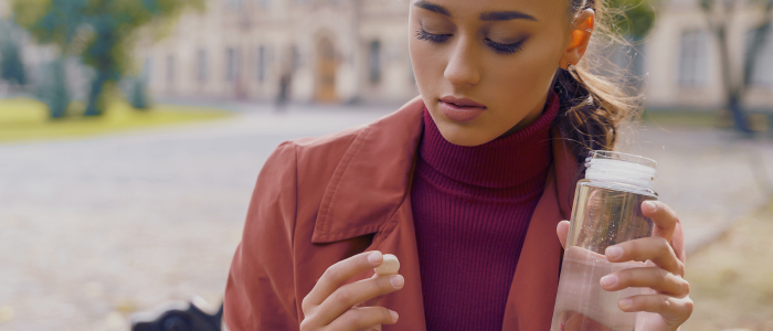 A woman is holding a water bottle and a pill.