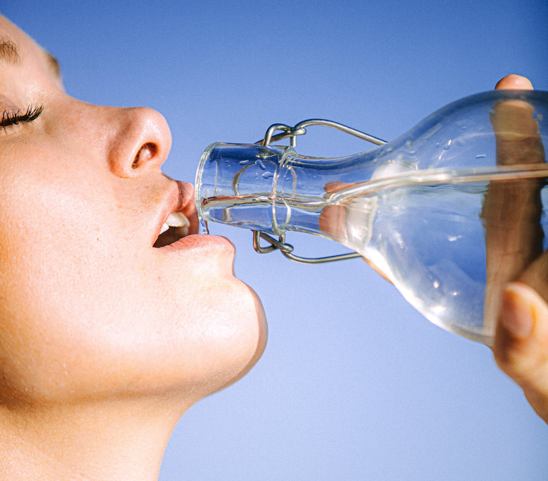 close up on female face drinking water from a glass bottle