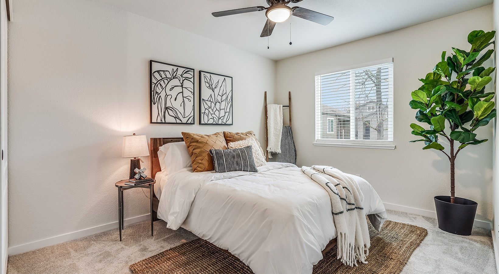 Bedroom with a bed, art, a plant, and a window. Neutral tones, natural light, and a casual, inviting feel.