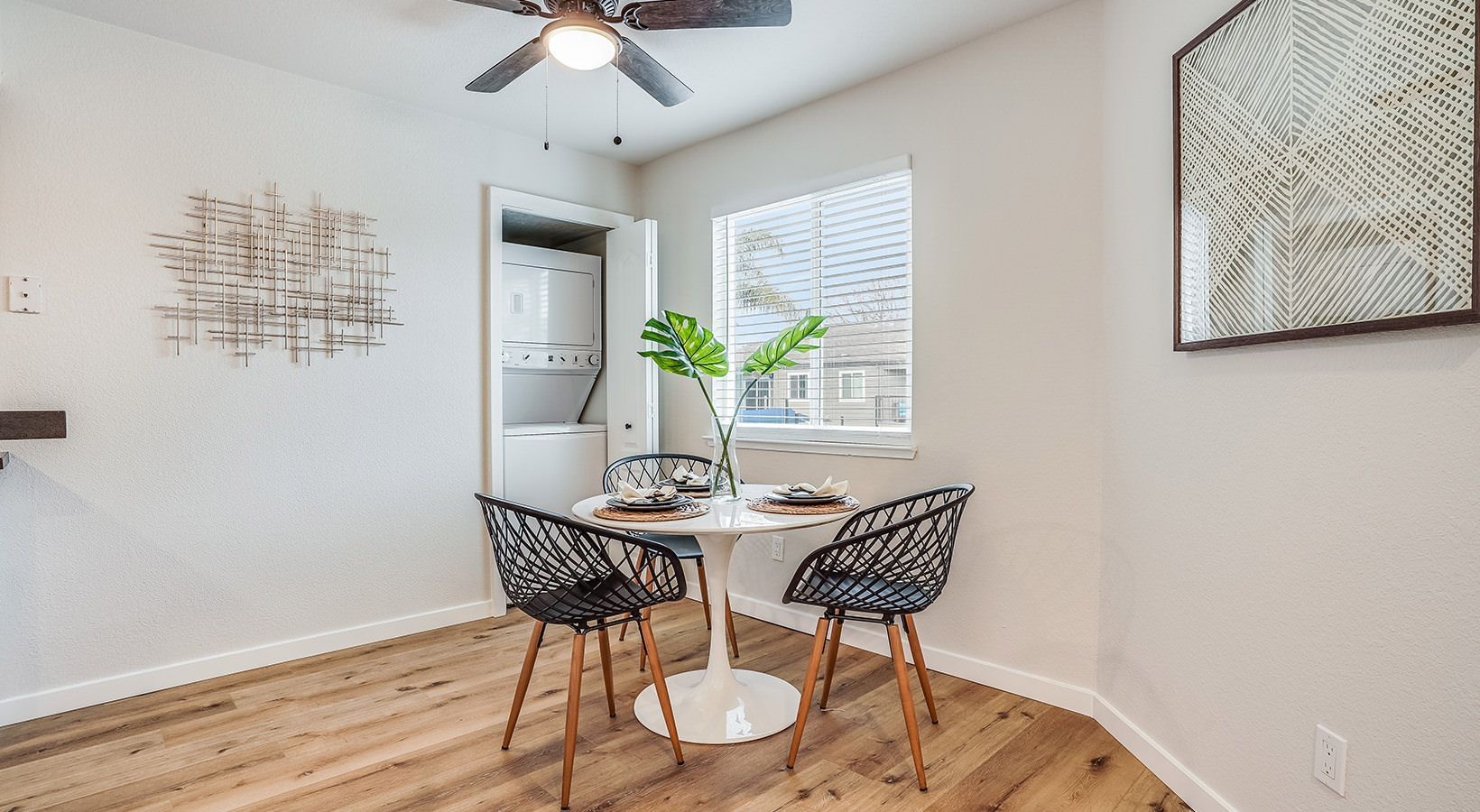 Dining area with small white table, black chairs, and a plant by the window.