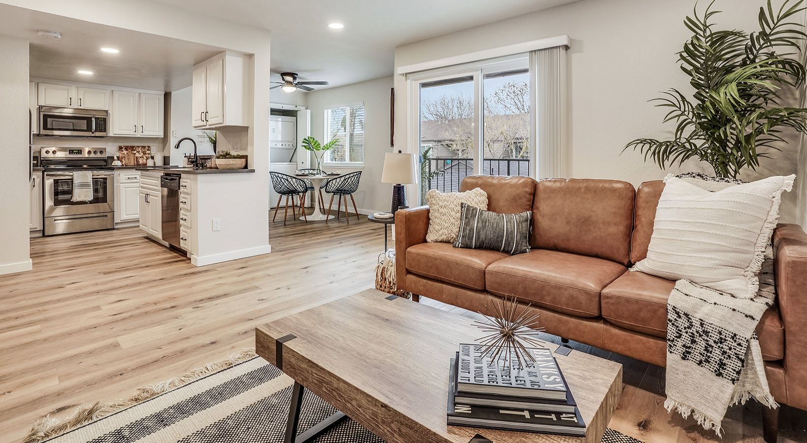 Living room with brown leather couch, light wood floors, and open kitchen.