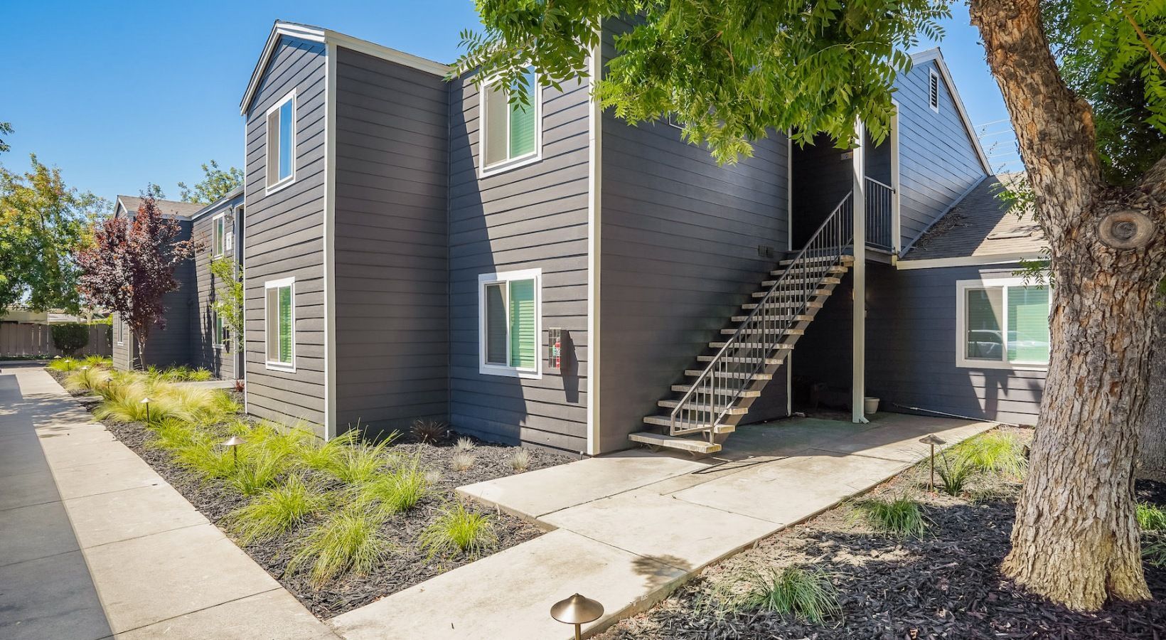 Two-story apartment building with dark gray siding, white-framed windows, and exterior stairs.