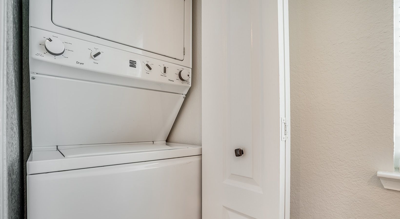 Stacked white washer and dryer in a laundry closet with a partially open white door.