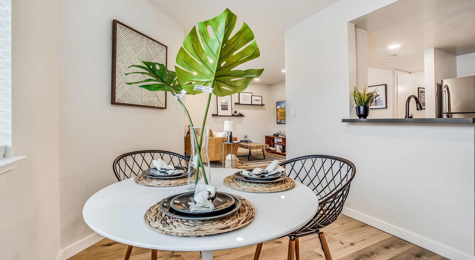 Dining area with round white table, wire chairs, and Monstera plant centerpiece.