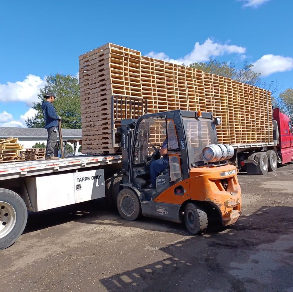 a yellow forklift is driving through a warehouse full of wooden pallets
