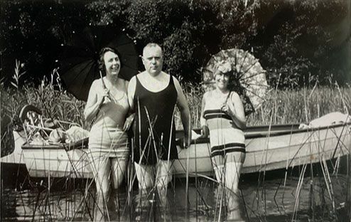 Auf einem Schwarzweißfoto stehen ein Mann und zwei Frauen neben einem Boot.