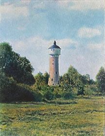 Ein Wasserturm steht inmitten eines von Bäumen umgebenen Feldes.