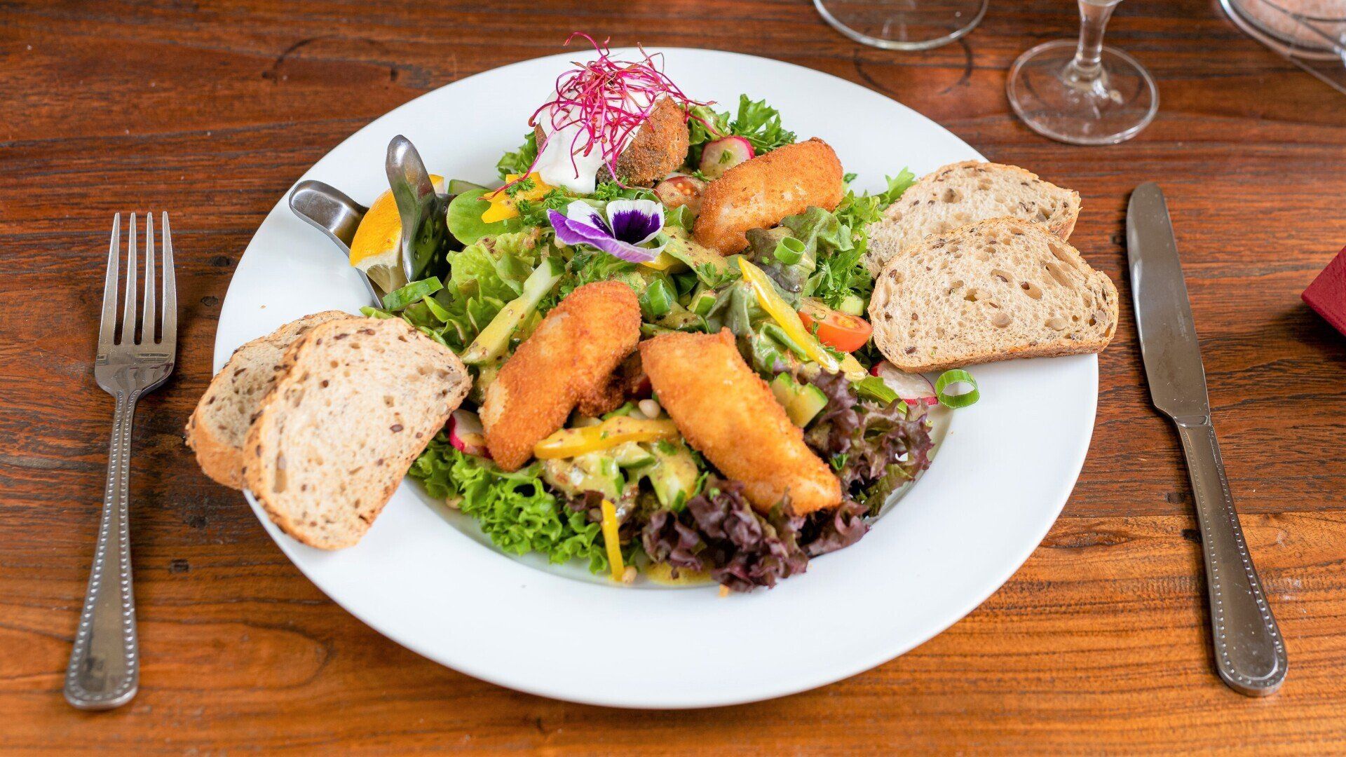 Ein weißer Teller mit Salat und Brot auf einem Holztisch.