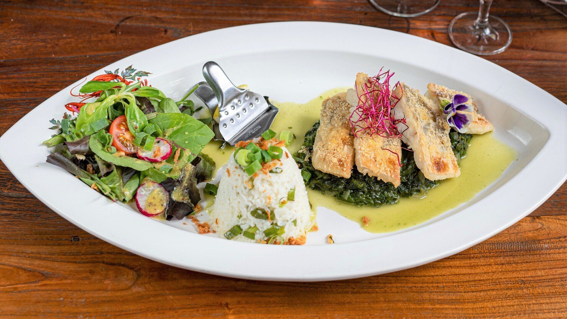 Ein weißer Teller mit Essen und einem Salat auf einem Holztisch.