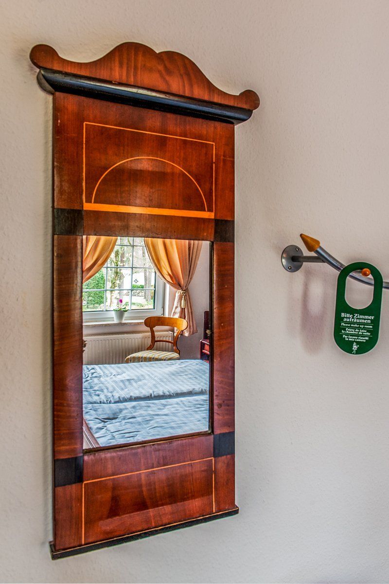 An einer weißen Wand neben einem Bett hängt ein großer Holzspiegel.