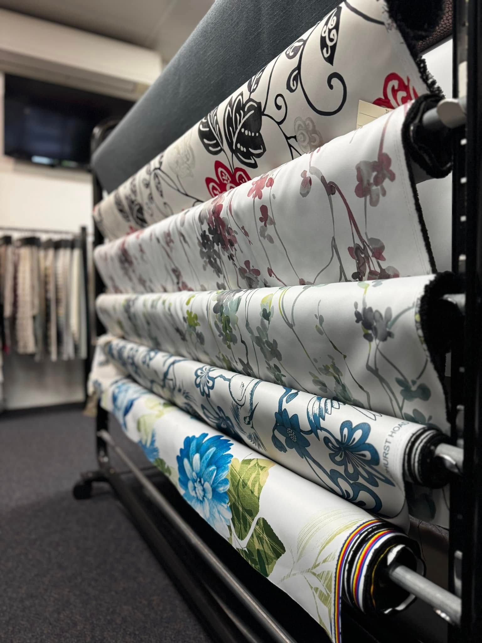 Multiple Rolls Of Decorative, Floral-patterned Fabric Arranged On A Tiered Metal Display Rack In A Store — Instyle Curtains & Blinds in Bungalow, QLD
