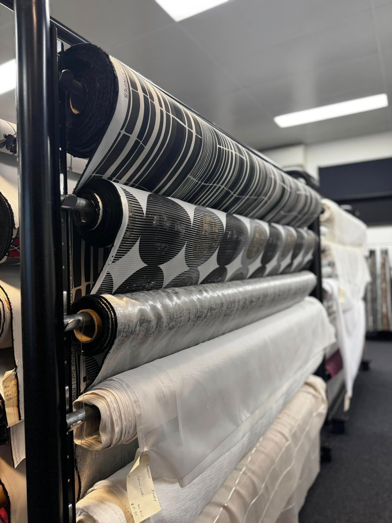 Fabric Rolls Of Various Patterns And Textures Stacked On A Storage Rack In A Retail Shop — Instyle Curtains & Blinds in Bungalow, QLD