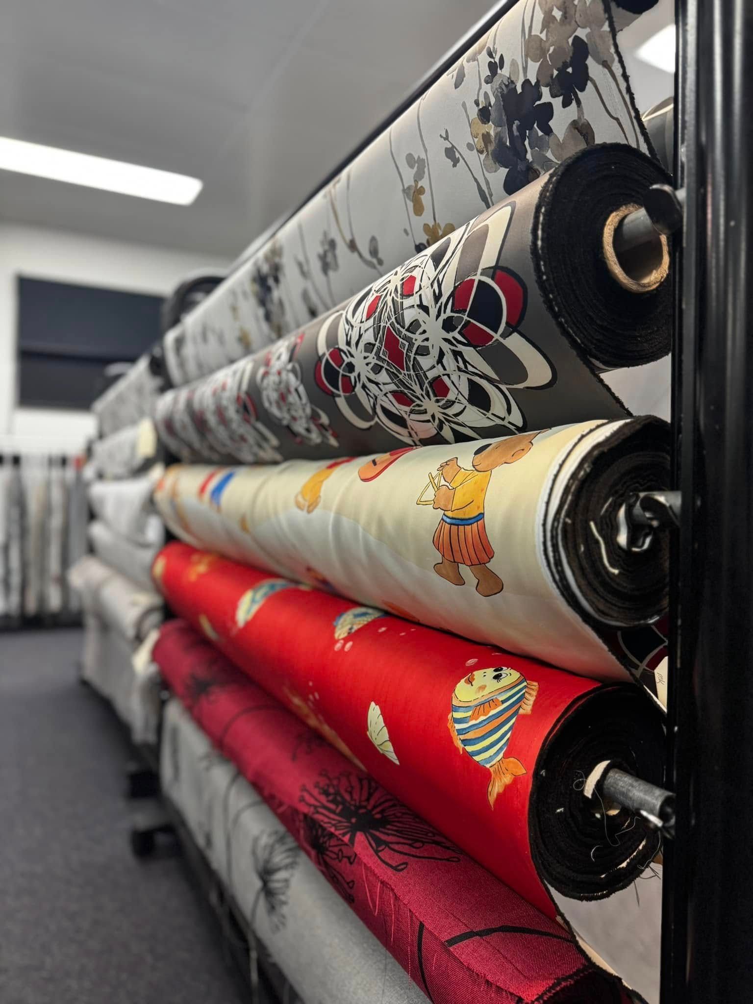 Fabric Bolts On A Rack With Various Patterns Including A White Floral, Dark Graphic, Cartoon Bear, And A Red Fish Print — Instyle Curtains & Blinds in Bungalow, QLD
