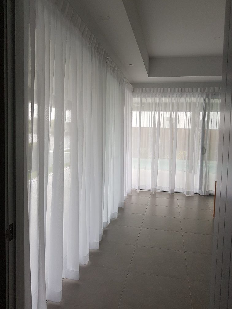 Sheer, floor-to-ceiling white curtains hanging in a modern room with tiled flooring and a view of an outdoor space  — Instyle Curtains & Blinds in Bungalow, QLD
