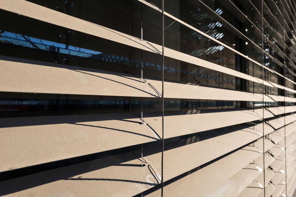 Black Blinds in a Window With a Tripod Lamp Beside It — Instyle Curtains & Blinds in Bungalow, QLD