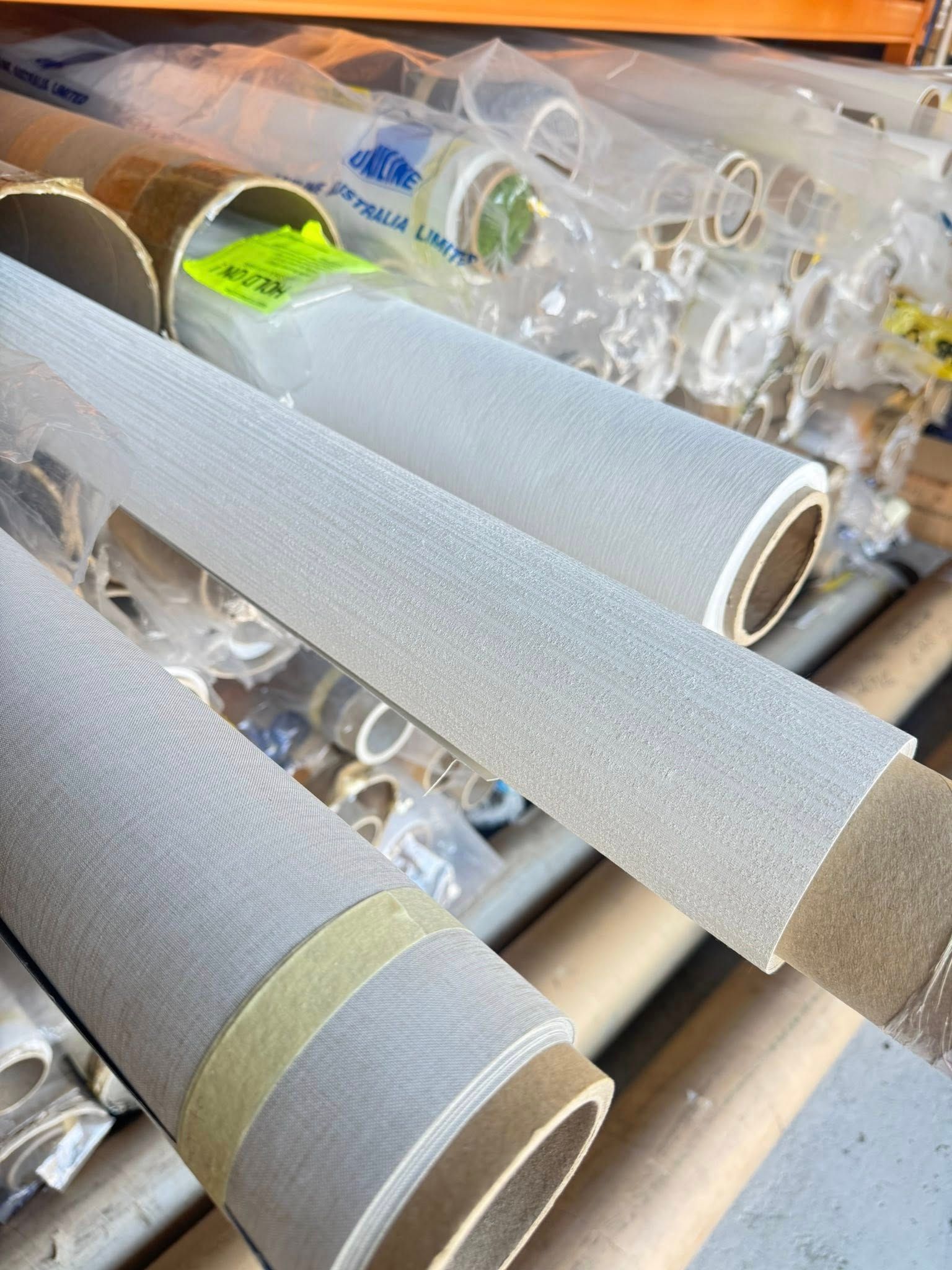 A Collection Of Tightly Rolled Fabric Bolts In Shades Of Gray, Stacked On Shelves In A Storage Or Warehouse Setting — Instyle Curtains & Blinds in Bungalow, QLD