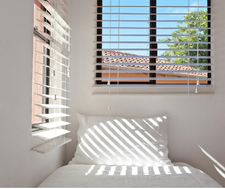 White Slatted Blinds Cast Shadows Onto a White Pillow and Bed — Instyle Curtains & Blinds in Bungalow, QLD