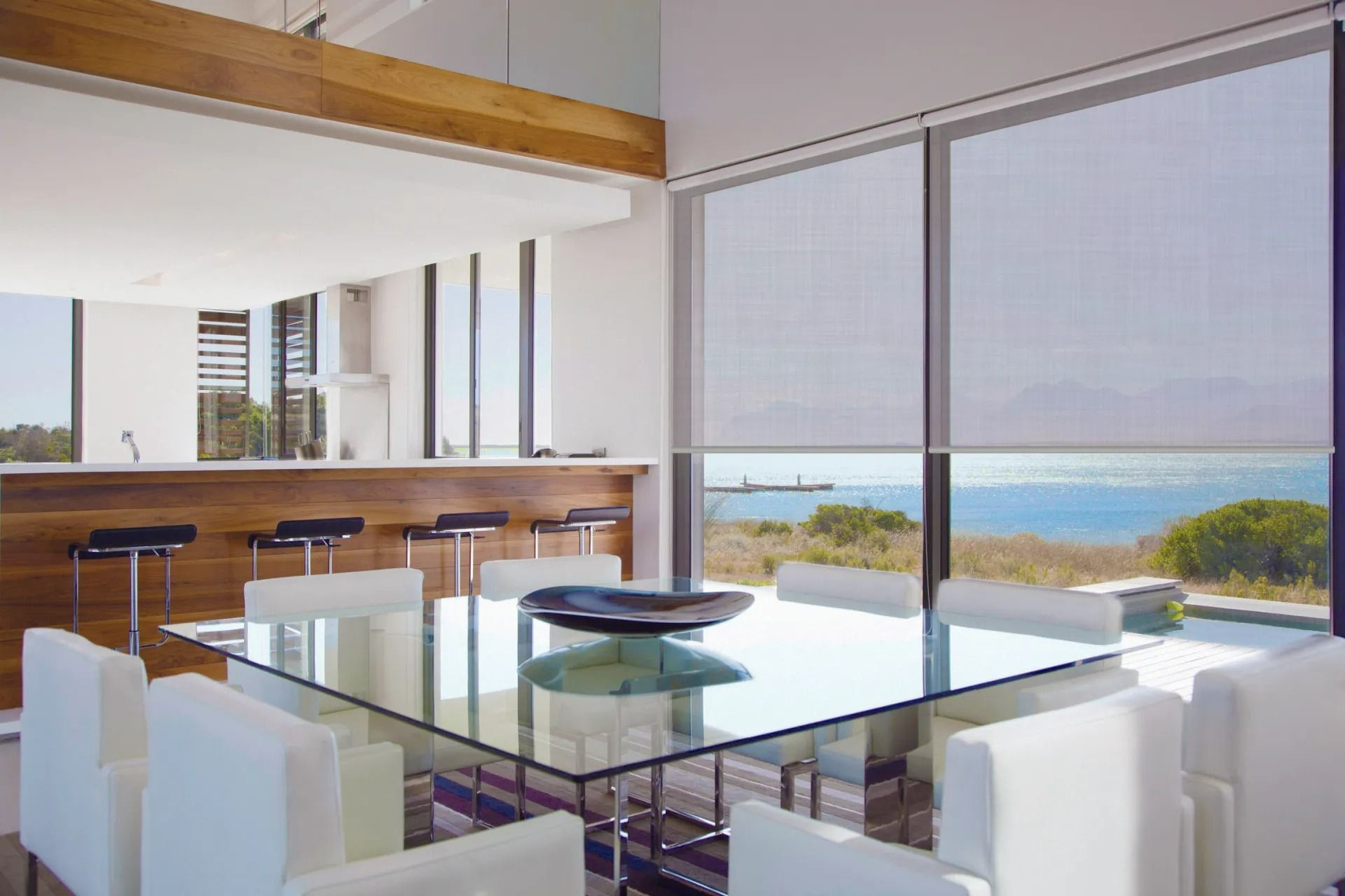 Dining Room With Glass Table, White Chairs, and Shades Overlooking Ocean — Instyle Curtains & Blinds in Bungalow, QLD