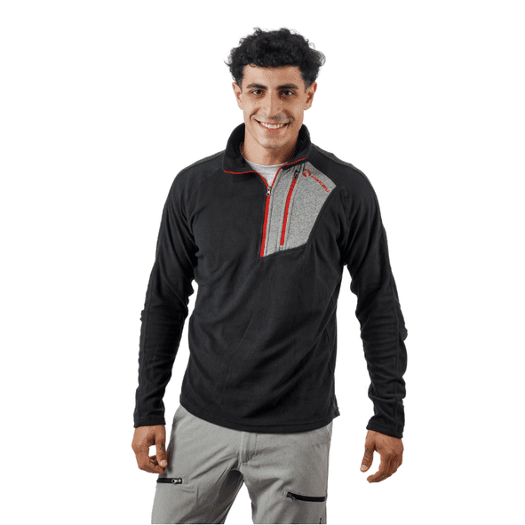 Hombre vestido con un forro polar negro con detalles rojos y pantalones grises, sonriendo.