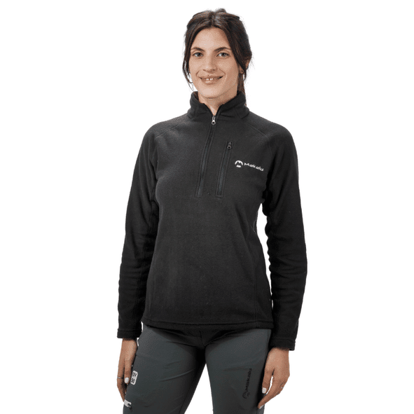 Mujer de pie, vestida con un forro polar negro con media cremallera y pantalones grises.