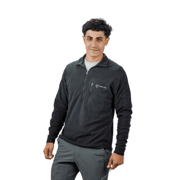 Hombre con camisa polar negra con cremallera, pantalones grises, sonriendo.