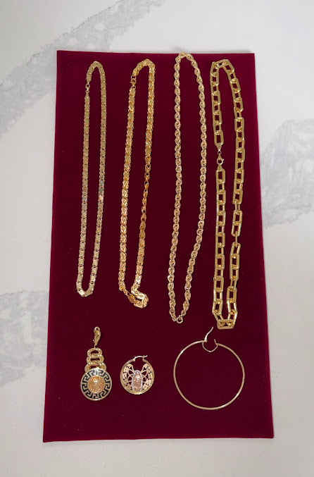 Assorted gold jewelry—necklaces, earrings, and a bangle—displayed on a red velvet background