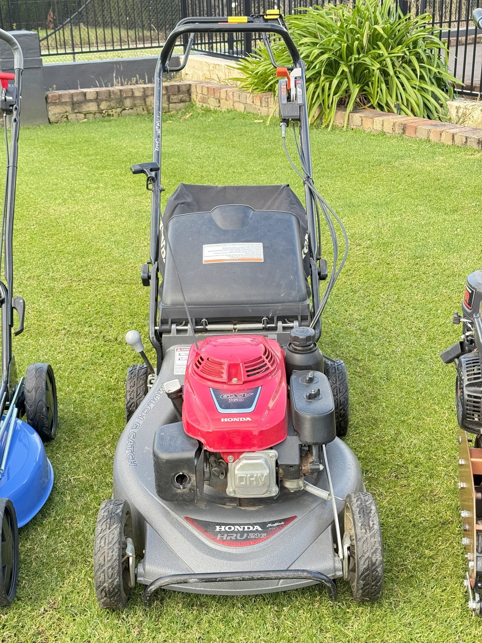 A red Honda lawnmower on green grass, positioned outdoors.