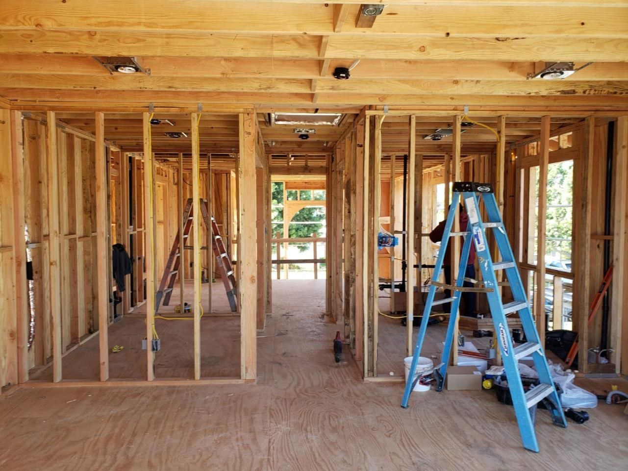 Unfinished house interior with wooden framing and a blue ladder on a plywood floor