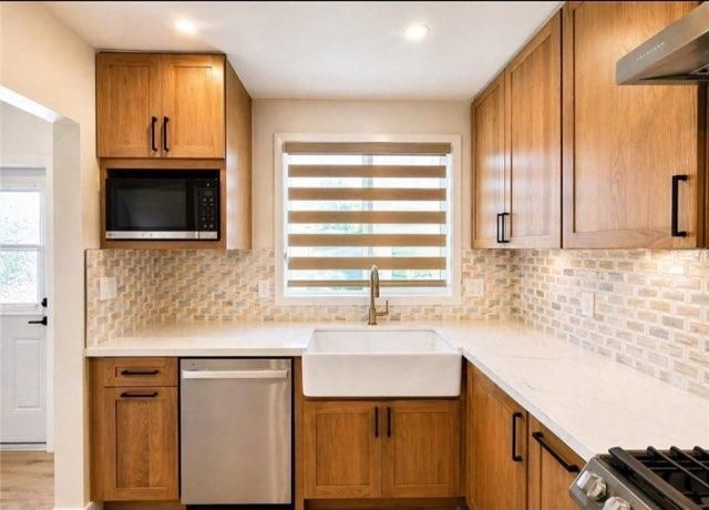 Modern kitchen with wood cabinets, white countertops, tiled backsplash, and a farmhouse sink