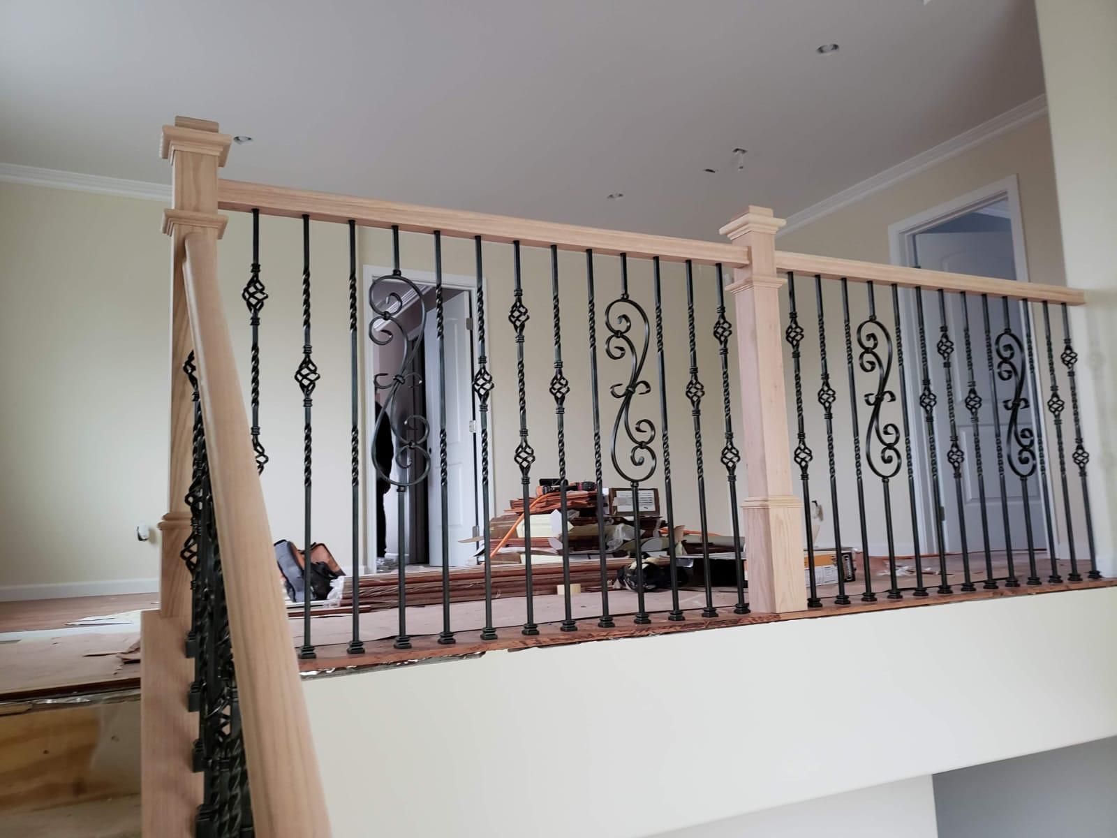 Indoor balcony railing with black wrought-iron balusters and light wood posts overlooking a living room