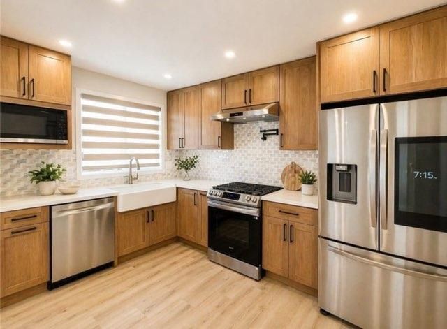 Modern kitchen with wood cabinets, stainless steel appliances, white countertops, and light wood flooring