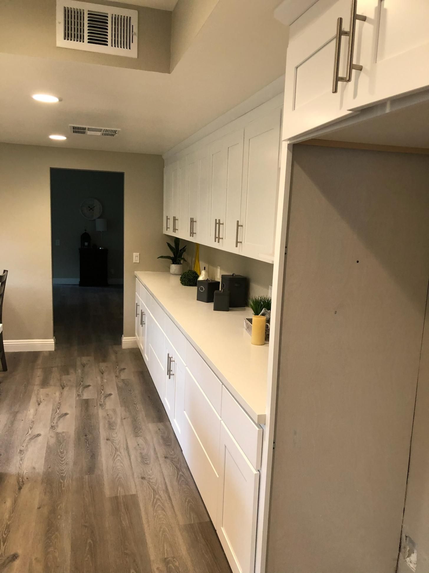 Narrow kitchen hallway with white cabinets, wood floors, and small potted plants on the counter.