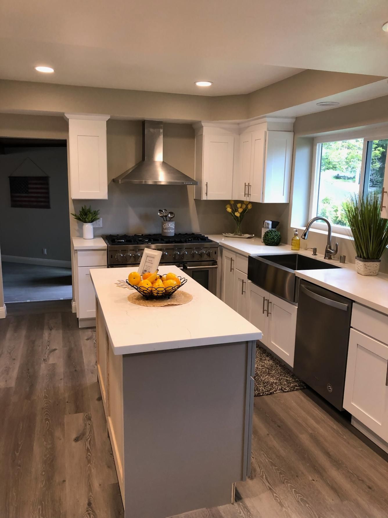 Modern kitchen with white cabinets, dark wood floors, stainless steel appliances, and a central island with fruit bowl
