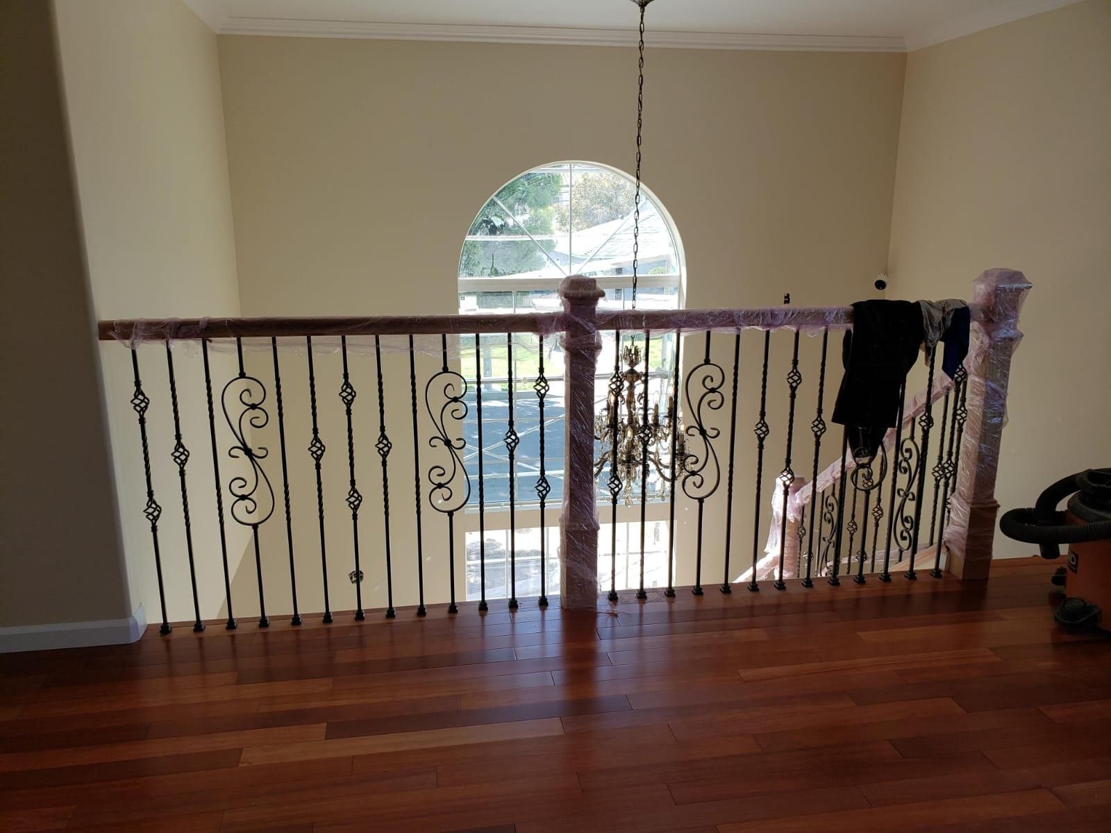 Indoor upstairs landing with wood floor, decorative railing, and arched window view