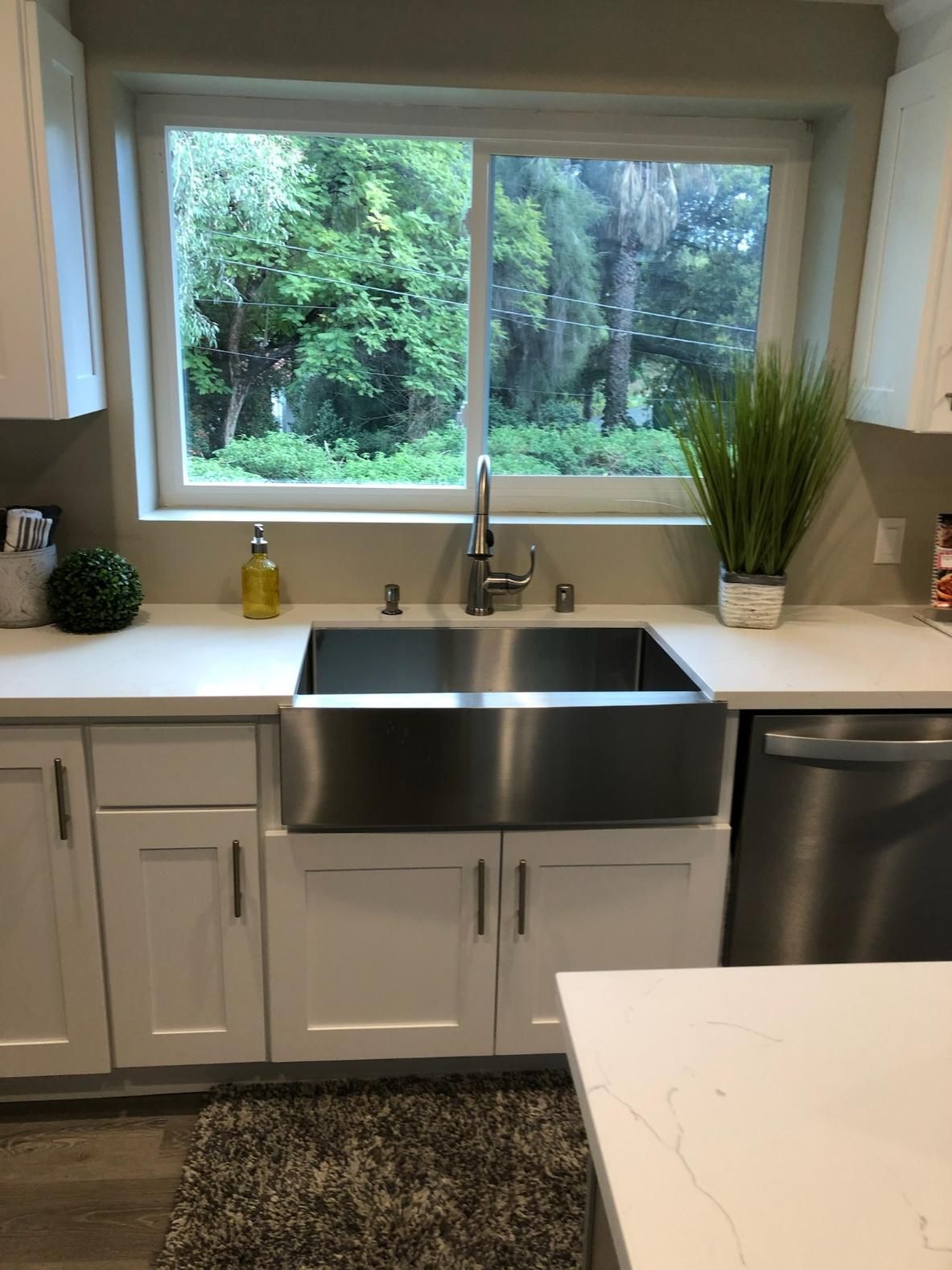 Modern kitchen sink under a large window with white cabinets, stainless steel faucet, and greenery outside.