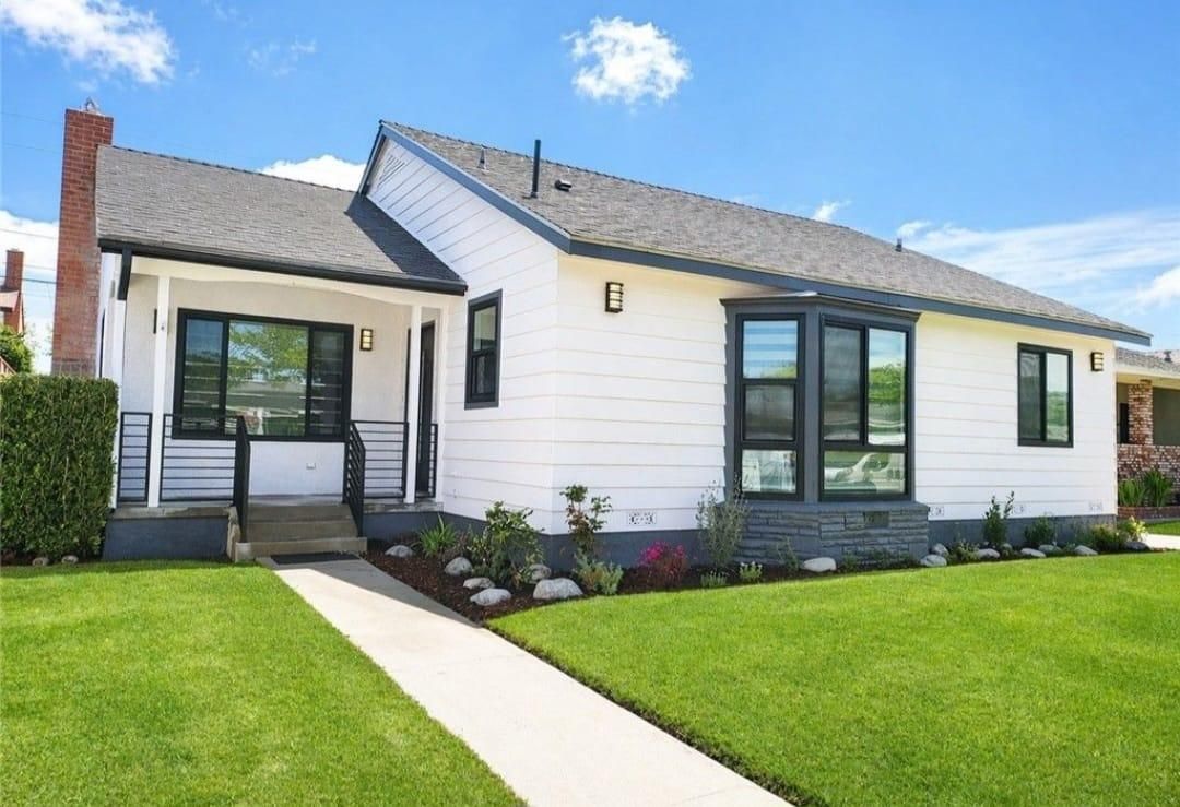 White single-story house with black trim, green lawn, and a front walkway under a blue sky