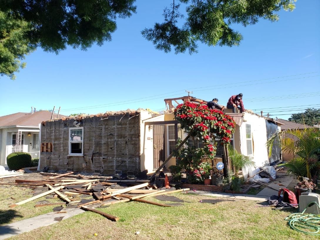 Damaged house with collapsed roof and debris in the yard under a bright blue sky