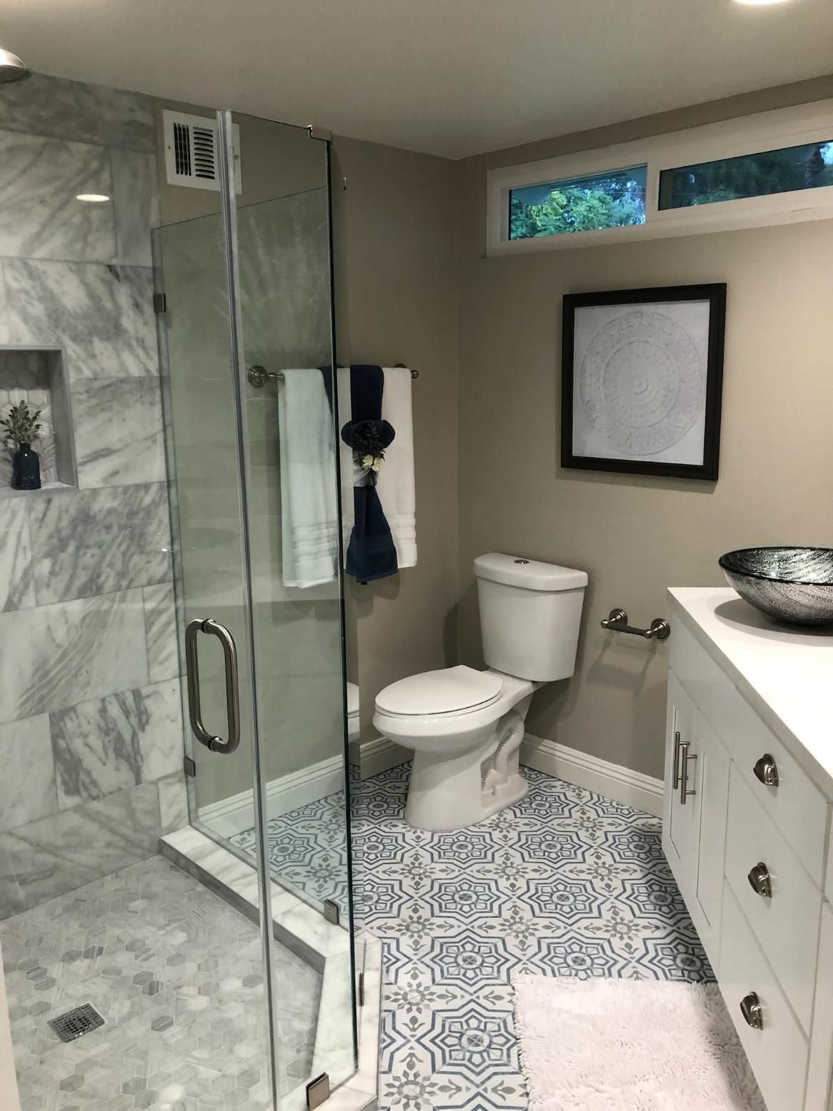 Modern bathroom with glass shower, toilet, patterned tile floor, and double vanity sink.