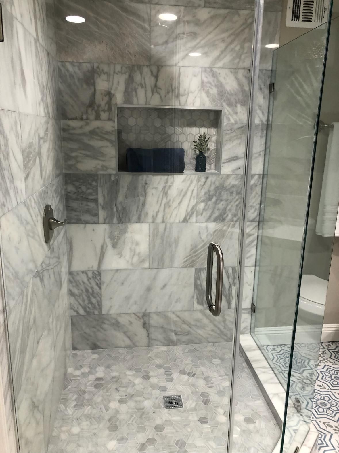Marble-tiled shower with glass door, built-in shelf, and wall-mounted grab bars