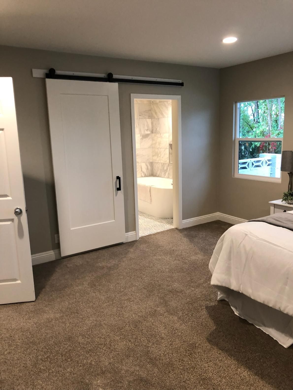 Bedroom with gray walls, sliding closet doors, open bathroom door, and a bed by a window.