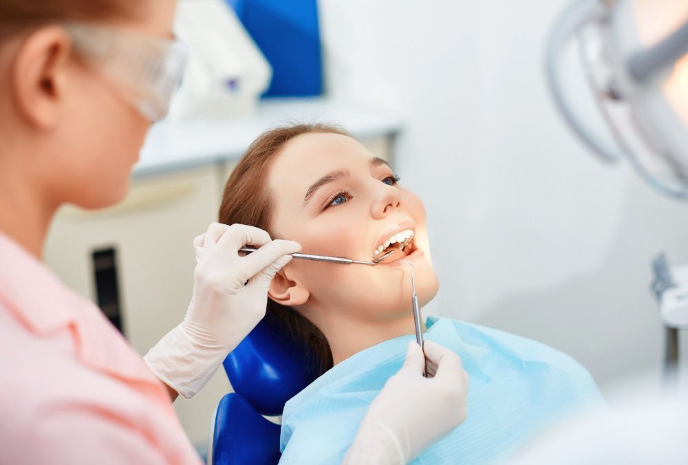 A woman is sitting in a dental chair getting her teeth examined by a dentist.