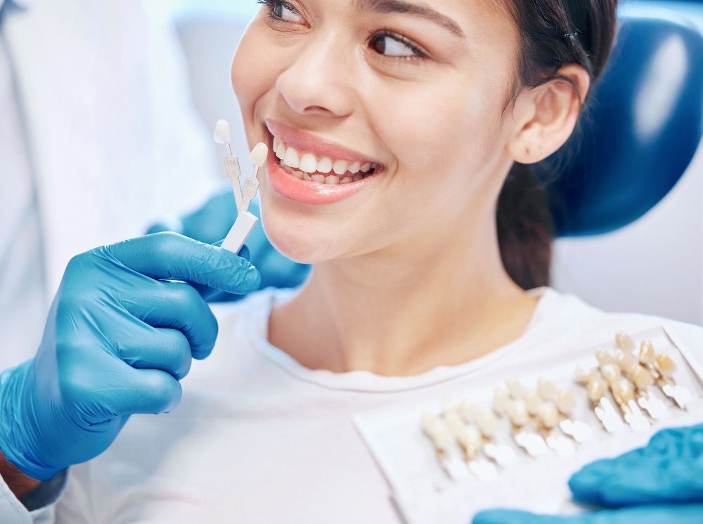 A woman is sitting in a dental chair while a dentist examines her teeth.