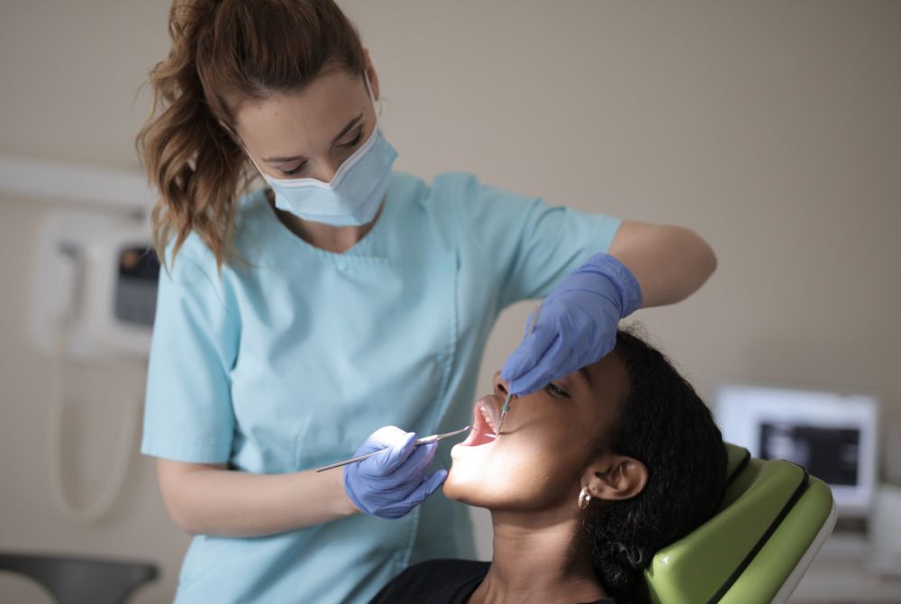 A woman is sitting in a dental chair while a dentist examines her teeth.