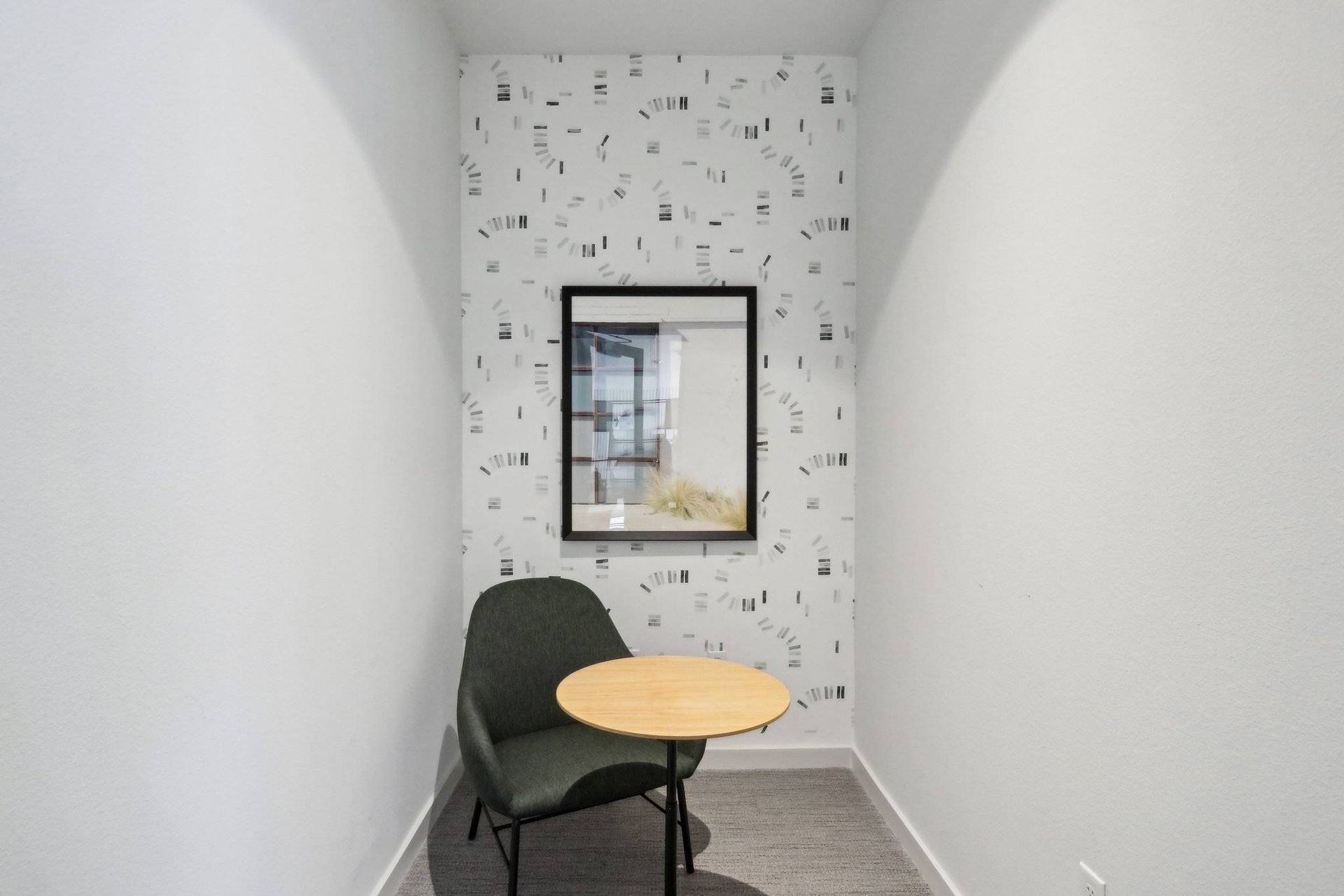 Small lounge nook with a round wooden table, dark chair, and framed wall art.