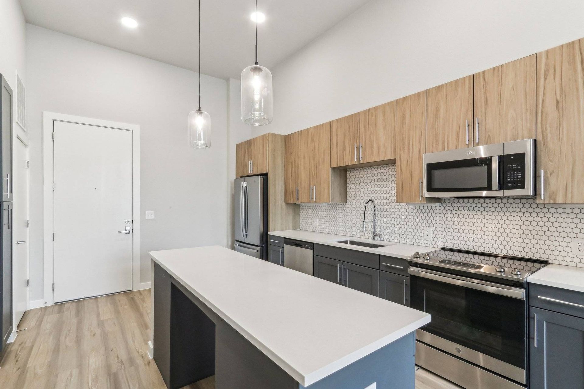 Modern apartment kitchen with an island, stainless steel appliances, and a white countertop.