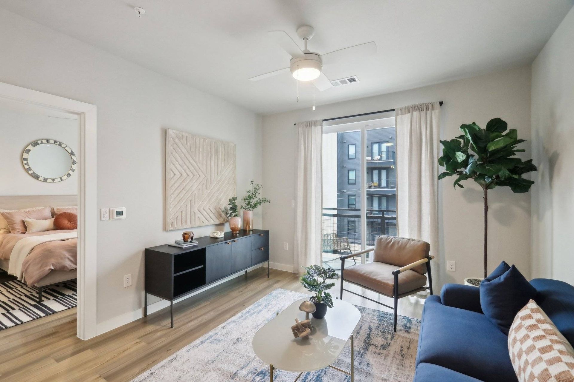 Bright living room in a modern apartment with a blue sofa, armchair, coffee table, and a balcony door.